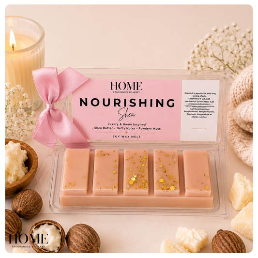 A clear plastic tray of six rectangular soy wax melts in a soft peach-pink color with scattered gold foil flakes, set under a pink and white product label. The scene is styled with a pink satin bow, a lit candle, whole and cracked walnuts, and dried flowers on a pale beige background.